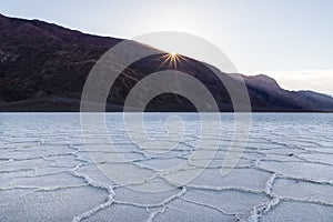 Sunrise over Badwater Basin, Death Valley, California. Sunburst over mountains in the distance; foreground covered with white salt