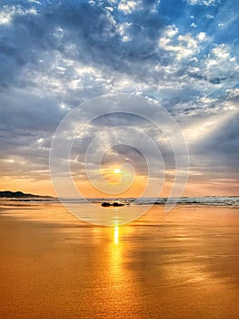 Sunrise over beach with blue cloudy sky and orange sand reflecting in the sun.