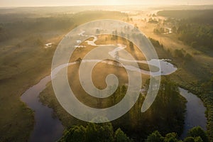 Sunrise over foggy river from above. Bright sunrays on misty river on meadow. Summer nature aerial view