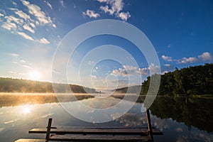 Sunrise over the foggy river with a wooden pier