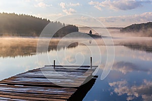 Sunrise over the foggy river with a wooden pier