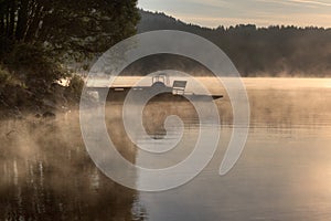 Sunrise over the lake in fog, pier and pedal boat, summer morning