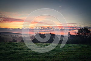 Sunrise over a neighboring forest with meadow in the foreground. Pasture landscape