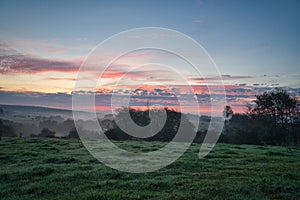 Sunrise over a neighboring forest with meadow in the foreground. Pasture landscape