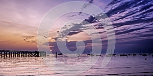 Sunrise over the ocean with silhouettes of a wooden pier and boats. Noirmoutier Island, France.