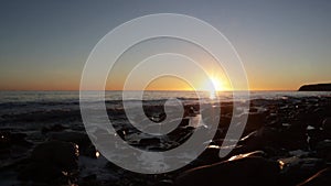 Sunrise over the sea viewed from a rocky beach with waves lapping against the shore