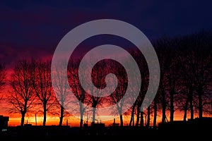 Sunrise over small town. Fiery dawn in the dark sky, horizontal photo. Silhouettes of trees and cars