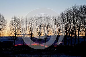 Sunrise over small town. Fiery dawn in the dark sky, horizontal photo. Silhouettes of trees, cars and industrial buildings