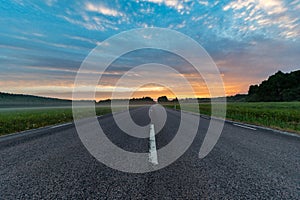 Sunrise over a straight road through green fields