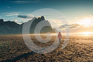 Sunrise over Vestrahorn mountain with a tourist man walking on black sand beach in summer