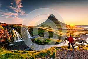 Sunrise over volcanic Kirkjufell mountain and photographer man standing in summer at Icelandnaefellsnes peninsula, Iceland