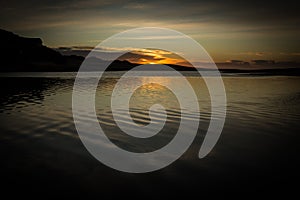 Sunrise over water with light reflecting on clouds