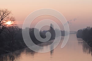 Sunrise over a waterway in Berlin at a misty morning with view to a bridge in background.