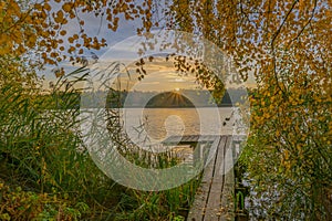 Sunrise over wooden pier on the lake. Wooden footbridge on the lake in the sunrise. A beautiful sunrise over lake greets the morni