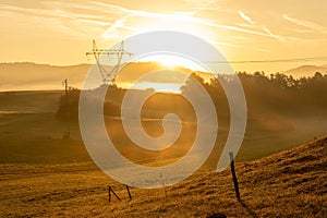 Sunrise over yellow meadows and powerline tower