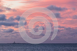 Sunrise with pink sky and clouds and a lighthouse in the horizon