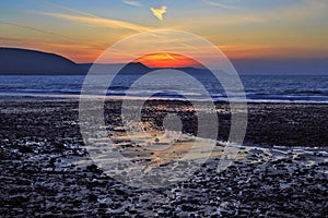 Sunrise reflected in the wet sand and pebbles of Freshwater East beach