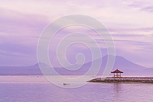 Sunrise on Sanur beach in Bali. Agung volcano in the dawn rays of the pink sun. Traditional gazebos on an artificial