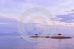 Sunrise on Sanur beach in Bali. Agung volcano in the dawn rays of the pink sun. Traditional gazebos on an artificial