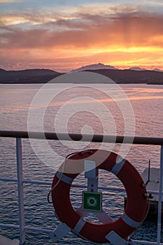 Sunrise on the Sardinian sea coast with intense orange color seen from the sea on the ferry that is about to dock with lifebuoy in