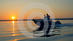 Sunrise scenery with two anglers driving a motorboat. Friendship, best friends concept.