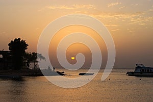 Sunrise on the sea. Silhouettes of the fishermen. A small boat near the shore. The colors of warm morning light