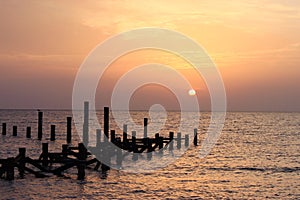 Sunrise on the sea. Wooden piles of destroyed pier sticking out of the water. The sun peeps out from behind the clouds. Red sea,
