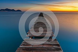 sunrise seascape with an old wooden dock leading out into the calm ocean waters of Alcudia Bay