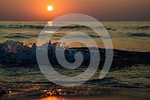 Sunrise at the shore of the sea and ocean, seen from the sand level, with the glowing wave of water, and pleasant bokeh