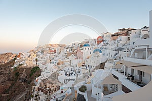 A sunrise shot of Oia village in Santorini island, Greece. Hotels and white buildings with blue dome churches in the background