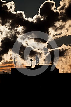 Sunrise with silhouettes of a communication antenna with satellite dishes on the roof of a skyscraper