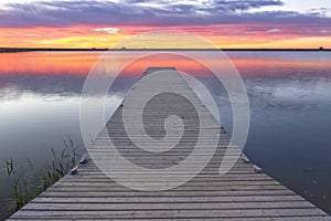 sunrise or sunset over a fishing dock with colorful clouds reflecting in the lake