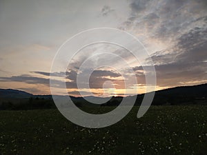 Sunrise or sunset over the hills and meadow.