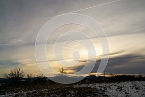 Východ nebo západ slunce nad kopci a loukou.