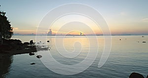 Sunrise Thailand aerial silhouette: woman rise up hands, stays on rocky beach near serene water