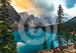 Sunrise with turquoise waters of the Moraine lake with sin lit rocky mountains in Banff National Park of Canada in