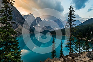 Sunrise with turquoise waters of the Moraine lake with sin lit rocky mountains in Banff National Park of Canada in