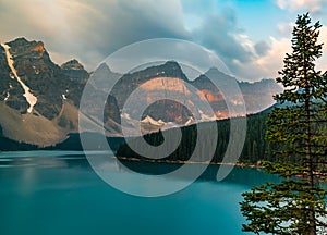 Sunrise with turquoise waters of the Moraine lake with sin lit rocky mountains in Banff National Park of Canada in