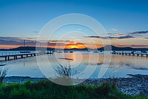 Sunrise waterscape with boats, wharves and sun coming over the mountain range