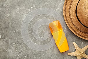 Sunscreen bottle with hat and shells on grey background. Cosmetics for safe sunburn. Top view, flatlay. Sun protection cream with