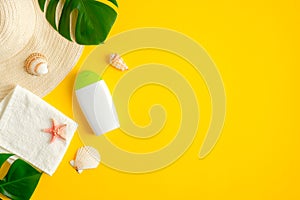 Sunscreen cream bottle, tropical leaves, towel, seashells on yellow background. Flat lay, top view. Sun protection, suntan