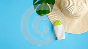 Sunscreen lotion bottle, green tropical leaf, female beach hat isolated on blue background. Sun protection, suntan cosmetics, skin