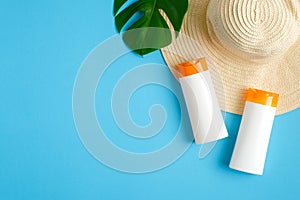Sunscreen lotion bottles, green tropical leaf, female beach hat isolated on blue background. Sun protection, suntan cosmetics,
