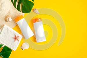 Sunscreen lotion bottles, tropical leaves, towel, seashells on yellow background. Flat lay, top view. Sun protection, suntan