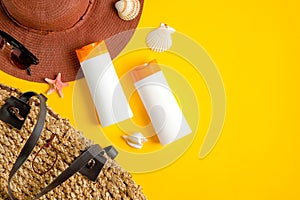 Sunscreen lotion in two white plastic bottles, sunglasses, beach hat and rattan bag on yellow background. Sun protection, sunblock