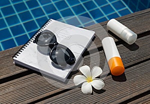 Sunscreen, planner, sunglasses and tropical flower near swimming pool