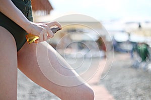 Sunscreen spray applying spf concept. Sunscreen suntan lotion in spray bottle. Young woman in spraying tanning oil on her leg from