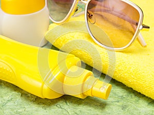 Sunscreen spray bottle, jar of sun cream, towel and sunglasses