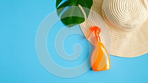 Sunscreen spray lotion bottle, green tropical leaf, female beach hat isolated on blue background. Sun protection, suntan cosmetics