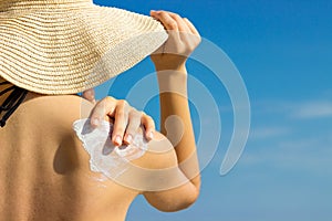 Sunscreen sunblock. Woman in a hat putting solar cream on shoulder outdoors under sunshine on beautiful summer day